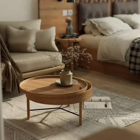 Styled studio corner combining a tufted-headboard bed with a small linen sofa and round wooden tray coffee table set on a patterned rug
