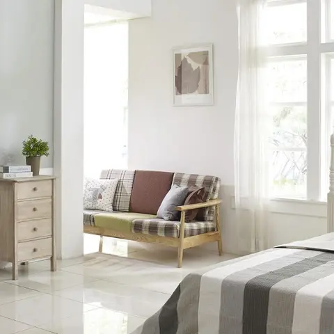Sun-bleached bedroom corner where a plaid-upholstered ash settee sits between a limed-wood four-drawer chest and the striped grey throw on a white turned-post