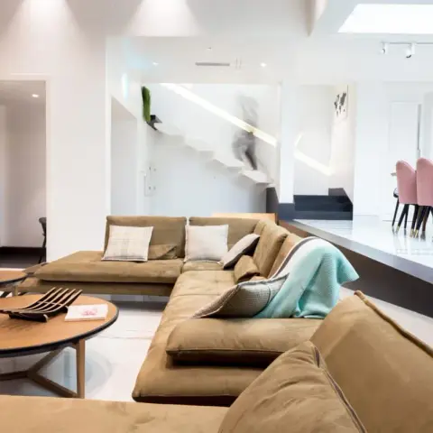 Sunken lounge with a deep tan suede modular sofa and two oval wooden coffee tables, a mint shell chair beside the black entrance door