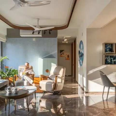 Sunlit apartment living room with two cream recliners and a round black nesting table on dark brown marble