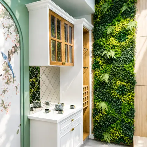 Sunlit balcony tea corner with a white panelled bar unit under a wood-framed glazed cabinet, a diamond-lattice mirror backsplash holding a painted tea