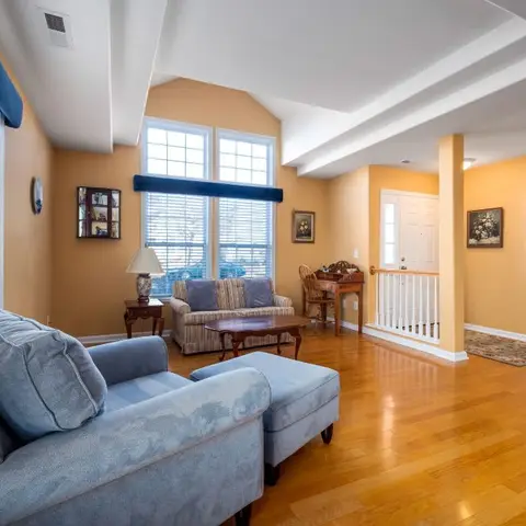 Sunny mustard-yellow living room with a vaulted tray ceiling, blue traditional-style sofa and armchair, and glossy hardwood floors leading to the entry.