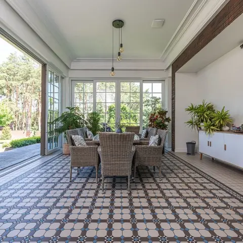 Sunroom dining area with a patterned tile floor, rattan dining chairs around a round table, a brick fireplace alcove, and glass doors opening to the garden.