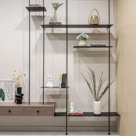 Suspended black metal shelving system styled with books, dried florals, and decor objects above a floating wood console, beside a fluted wall panel.