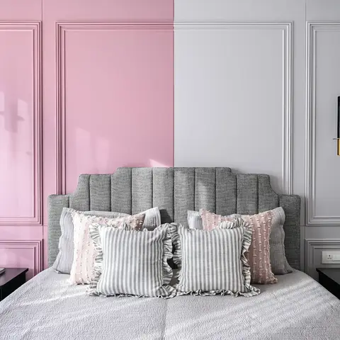 Symmetrical bedroom with a split pink-and-grey moulded panel headboard wall and matching marble-capsule pendant lights on either side of a channel-tufted grey