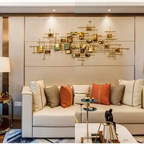 Symmetrical cream living room with a gold abstract sculptural wall art piece centered above twin sofas with rust and patterned cushions