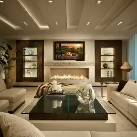 Symmetrical living room built around a long pebble-bed gas fireplace with the TV recessed above it, flanked by two lit dark-veneer display niches