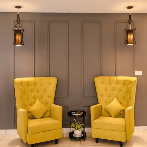 Symmetrical living-room vignette: two mustard button-tufted high-back wing chairs flanking a small black two-tier round table