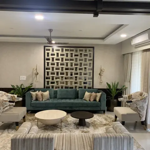 Symmetrical living room with a teal velvet buttoned sofa under a bevelled mirror-grid panel flanked by brass globe sconces, floral tub chairs with ottomans