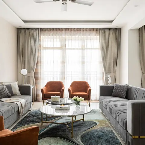 Symmetrical living room with two channel-tufted grey velvet sofas facing each other, rust velvet armchairs at both ends, a round marble-and-brass coffee table