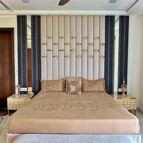 Symmetrical master bedroom with a full-height channel-tufted beige headboard wall studded with staggered brass straps