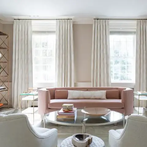 Symmetrical sitting room with a blush velvet tuxedo sofa centred between two tall sash windows, a round mirrored coffee table