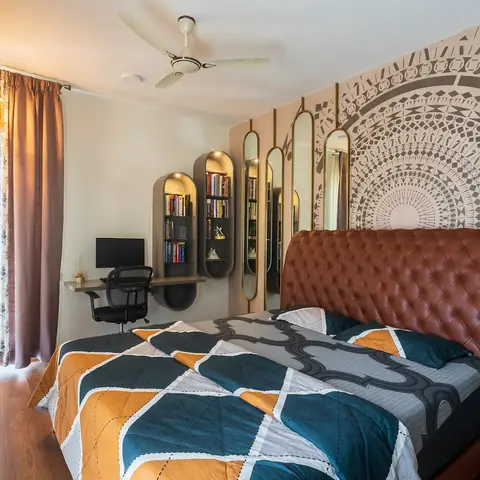 Tan tufted-leather bed set against a grey-on-blush mandala mural, with arched brass mirrors, capsule-shaped book niches and a wall-hung desk beside it.