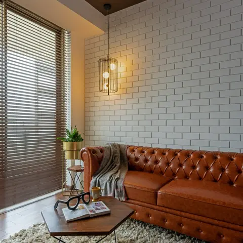 Tan tufted leather chesterfield sofa against a white brick-clad wall with a black cage pendant light and hexagonal wood coffee table