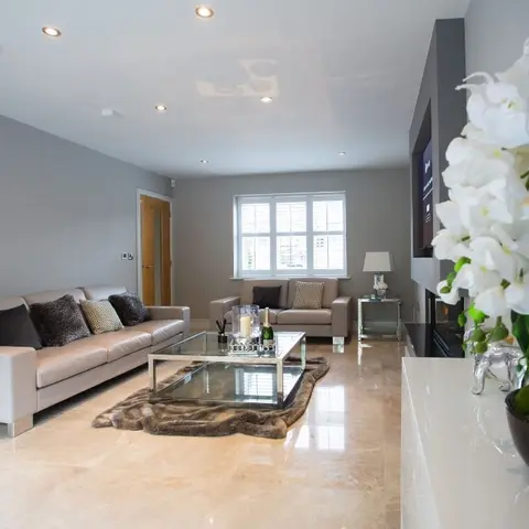 Taupe leather sofa set around a mirrored glass coffee table on a faux-fur rug, with a wall-mounted TV media unit and a large white orchid arrangement in the