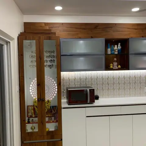 Teak-framed pooja mandir with etched-glass shutters carrying a Sanskrit shloka and a sunburst motif