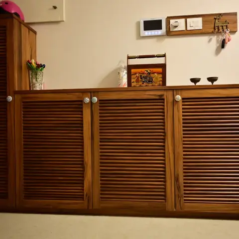 Teak louvred shoe cabinet at a flat entrance, stepping up to a taller unit on the left, with blue-and-white ceramic knobs