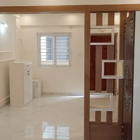 Teak slat jaali screen with white display boxes standing between the main door and a marble-tiled foyer
