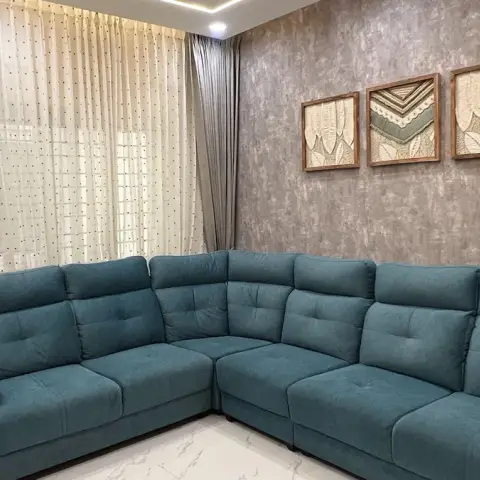 Teal fabric L-shaped sofa filling a compact living room against a grey textured feature wall hung with three teak-framed textile artworks
