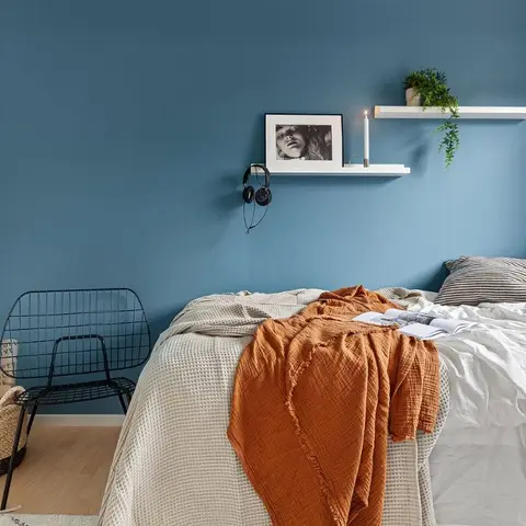 Teal-painted bedroom wall carrying two slim white picture ledges with a framed portrait, a lit candle and a trailing plant
