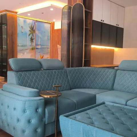 Teal quilted sofa, armchair and ottoman filling a just-handed-over living room, backed by a fluted brass-framed screen