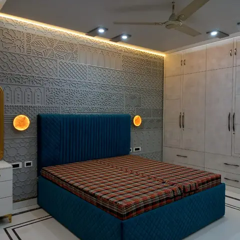 Teal quilted velvet bed with a tartan-patterned cover, set against a heavily textured 3D-carved geometric wall panel with round backlit wall sconces