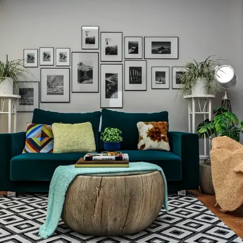 Teal velvet sofa under a salon-hung grid of black-and-white landscape prints, with a solid timber-stump drum table on a black diamond kilim rug