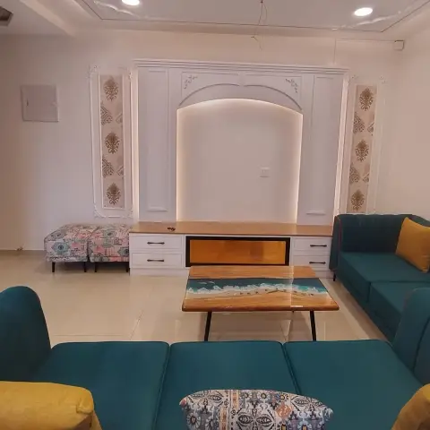 Teal velvet sofas with mustard bolsters and an ikat cushion sit around an epoxy-river wooden table