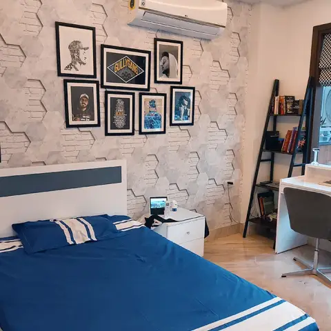 Teen bedroom with a hexagon-textured accent wall, a gallery wall of framed rap-artist prints, and a navy-and-white striped bed set beside a corner study desk.