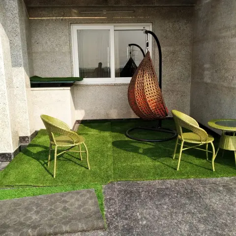 Terrace corner laid with artificial turf against granite-clad walls and pergola beams