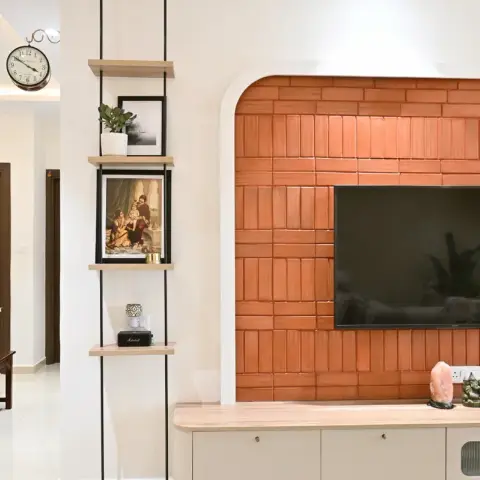 Terracotta brick-tile TV wall set inside a white arched niche, with a light-oak floating console and a suspended four-tier shelf carrying a Ravi Varma print