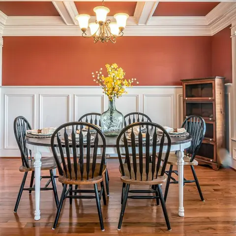 Terracotta-walled dining room with white raised-panel wainscoting, black windsor chairs around an oval table, and a coffered wood ceiling.
