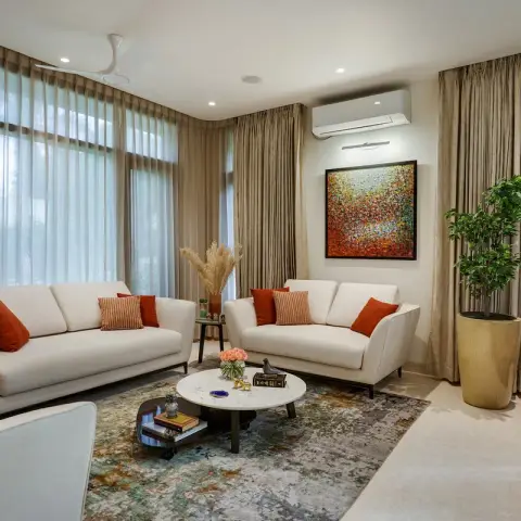 Three cream sofas set around a round white-marble coffee table on a mottled teal-and-rust rug, the same rust bolsters repeated on every seat