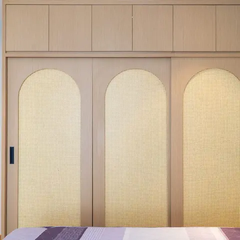 Three sliding wardrobe shutters in pale oak with tall arched cane-webbing inserts, a matching oak oval mirror on the pale blue side wall