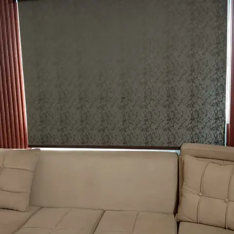 Tight crop of a beige tufted sectional sofa against a window with a roller blind and fluted maroon wall panelling