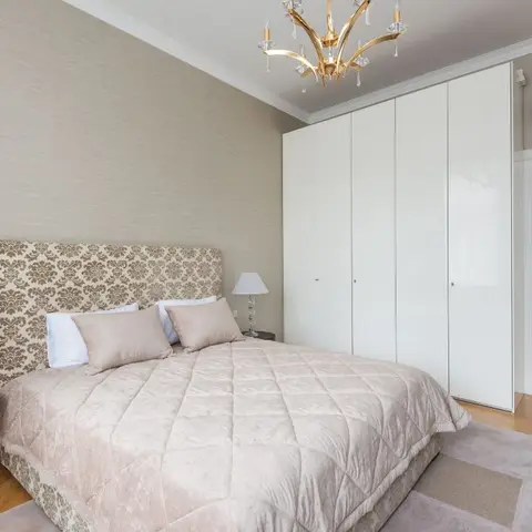 Traditional bedroom with a damask-upholstered headboard, a gold crystal chandelier, and a full-height glossy white wardrobe.