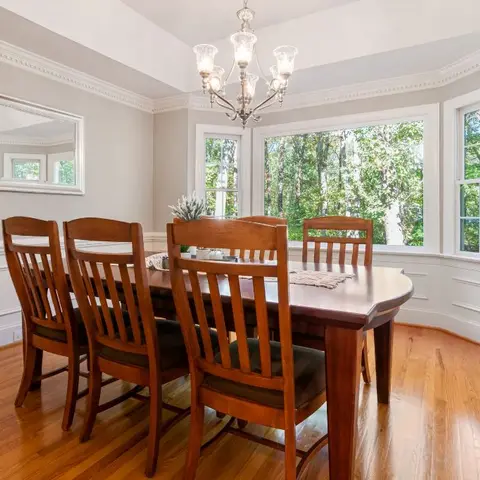 Traditional dining room with a bay window, crown moulding and wainscoting, a wood dining table seating six, and a crystal chandelier.
