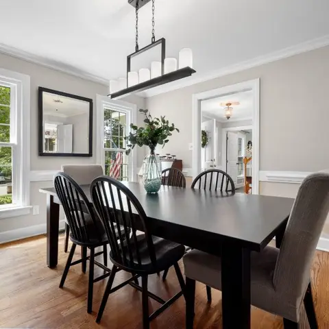 Traditional dining room with a black wood table and mixed spindle-back chairs beneath a candle-style linear chandelier, framed by chair-rail wall moulding