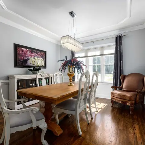 Traditional dining room with a crystal box chandelier over a wood trestle table, ivory upholstered chairs