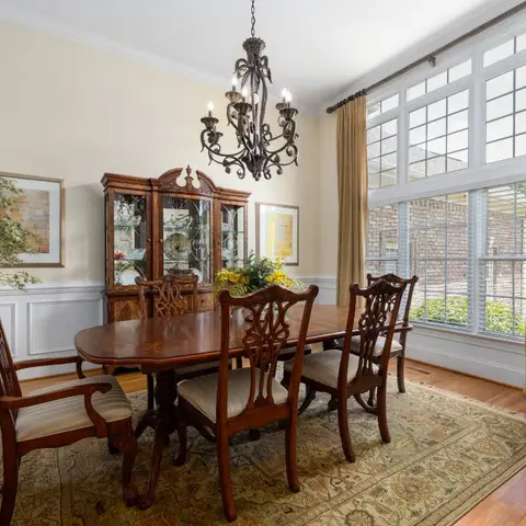 Traditional dining room with a mahogany pedestal table and carved chairs beneath a wrought-iron candle chandelier, a glass-front china cabinet