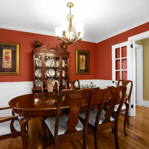 Traditional dining room with deep red walls above white wainscoting, a dark wood oval table with six chairs, and a glass-front china cabinet in the corner