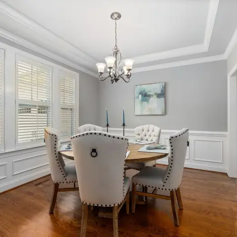 Traditional dining room with wainscot panelling, a round wood table, nailhead-trim upholstered chairs and a candelabra chandelier.