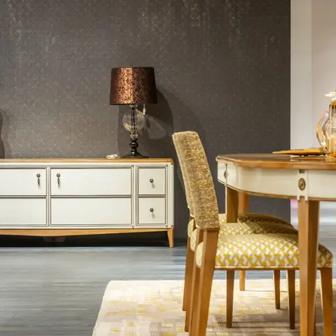 Traditional dining vignette with an oval wood dining table and geometric-patterned upholstered chairs beside a cream wood sideboard with brass hardware and a