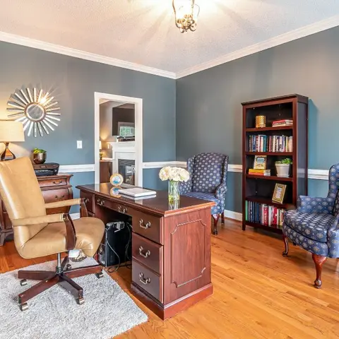 Traditional home study with blue-grey wainscoted walls, a wood desk, wingback chairs and a mahogany bookcase.