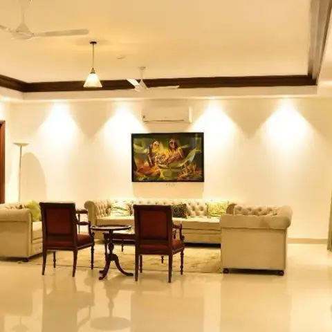 Traditional Indian living room with dark wood cove-ceiling trim, a large framed painting over tufted cream sofas, and a wooden curio cabinet
