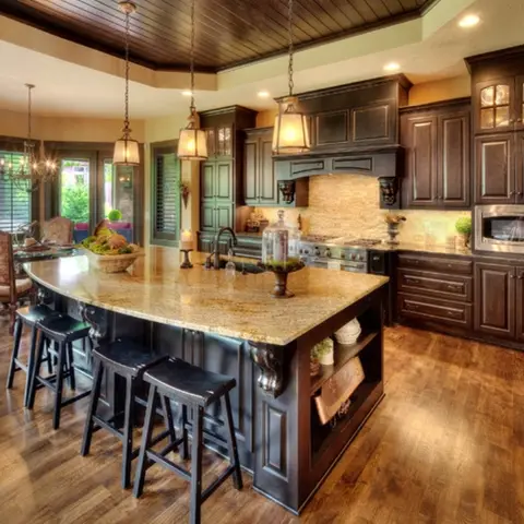 Traditional kitchen with a dark wood island topped in gold-veined granite, carved corbels, three lantern pendants and a wood-plank tray ceiling