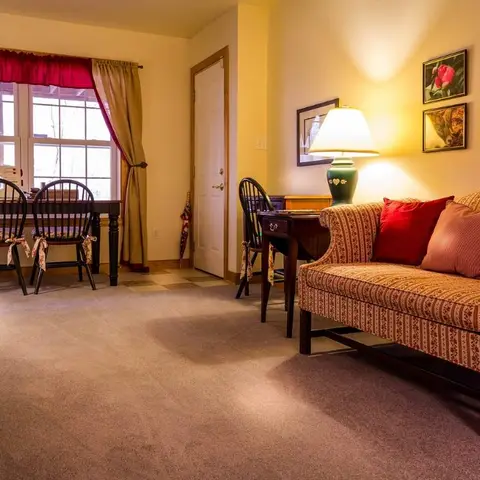Traditional living/dining room with a red-striped floral sofa and burgundy throw pillows, bow-tied Windsor chairs, a gallery wall of framed photos