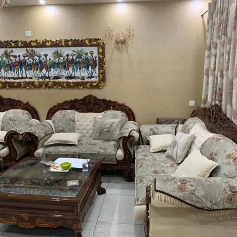 Traditional living room with a carved dark-wood sofa set upholstered in floral tufted fabric, a large gilt-framed folk-art painting