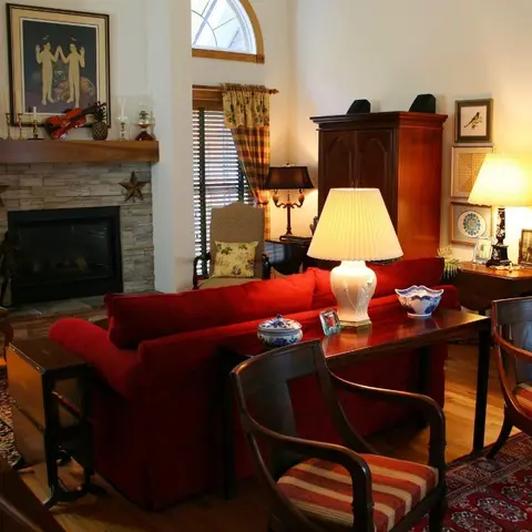 Traditional living room with a stacked-stone fireplace, a deep red sofa flanked by antique wood cabinets, and a richly patterned area rug.