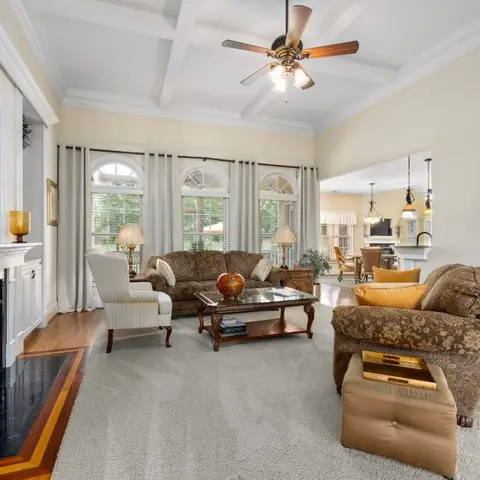 Traditional living room with a white fireplace mantel, a coffered ceiling with a wood-blade fan, floral upholstered sofas around a glass-top wood coffee table